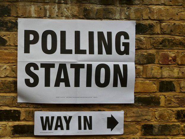 Image of a polling station sign on a brick wall with Way in sign underneath