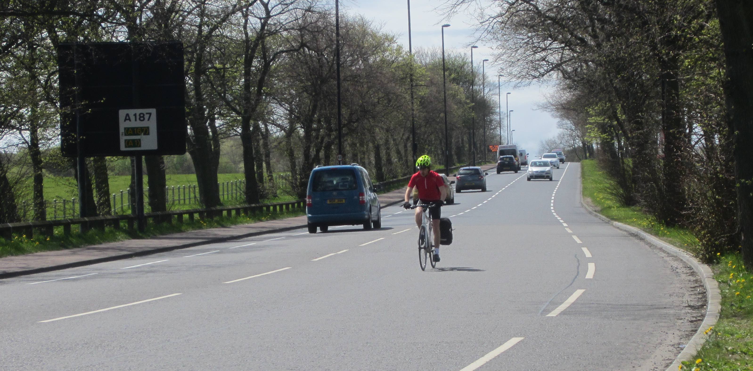 Person cycling in the main carriageway approaching the Kenton Road traffic lights.