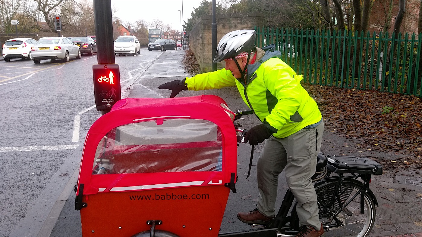 Picture of a cyclist with an adapted cycle trying to reach the button on a Pelican crossing.