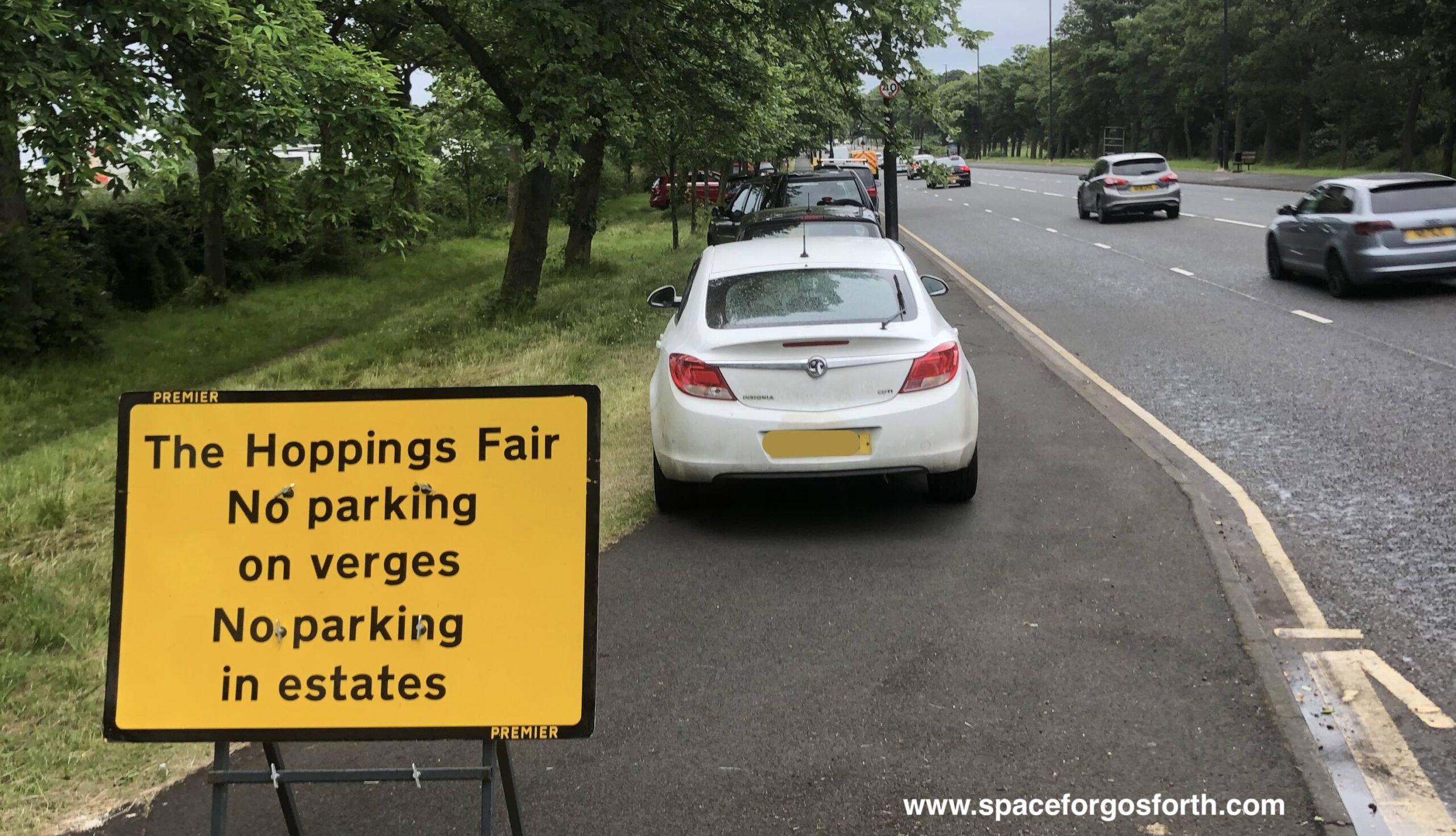 Vehicles parked on the pavement in front of a 'no parking on verges' sign