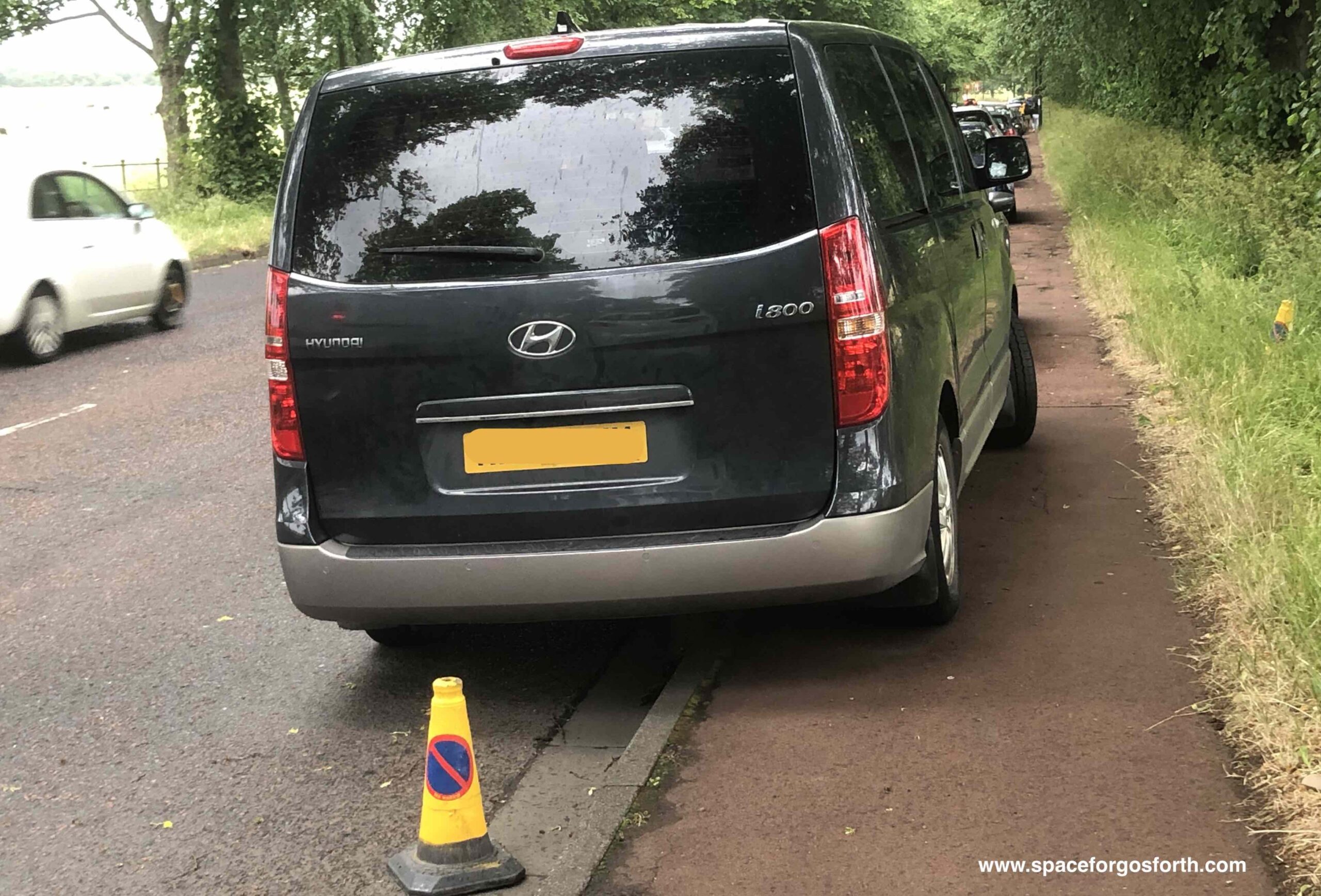 Vehicle parked on the pavement in front of a 'no parking' traffic cone